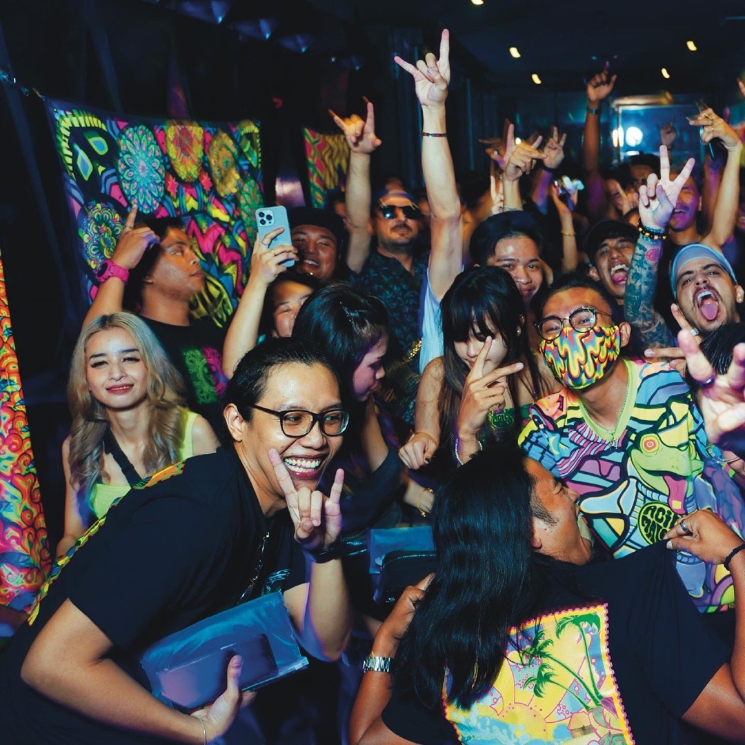 Crowd throwing their hands up in front of glowing Acid Malaya artwork